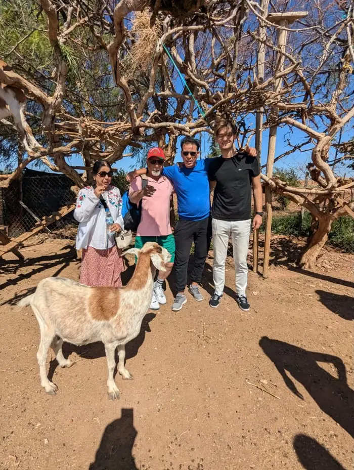 Guests and guide with a goat at a roadside argan farm